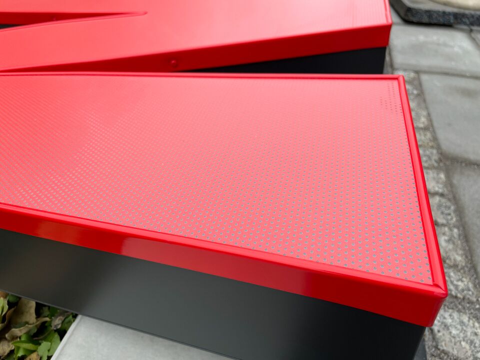 Ein roter 3D-Buchstabe, der mit Lochfolie beklebt ist, wird aus einer seitlichen Perspektive gezeigt.